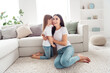 © deagreez - Mother and daughter sharing a secret whisper in a bright living room, playful family moment of affection and bonding at home