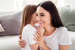 © deagreez - Mother and daughter sharing a secret hug and smile in a cozy living room, affectionate family bonding and parenting moment at home