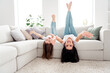 © deagreez - Mother and daughter laughing and playing upside down on a couch in a bright living room at home, happy family moment and playful bonding