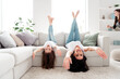 © deagreez - Mother and daughter laughing and hanging upside down on living room sofa during playful family moment at home