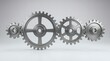 © Candra - Four interlocking metallic gears in a horizontal row representing teamwork and mechanics.