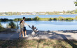 © Anna - Young parents stroll with a stroller through a park next to a lake. The family is enjoying a walk together in nature on a summer day.
