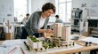 © Chandara - A woman in a gray sweater and blue pants is working on a model of a building in an office setting.