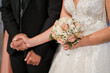 © Konstantinos - Close up of bridal bouquet with pink roses, bride and groom holding hands at Christian wedding ceremony
