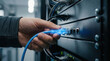 © weerasak - Hand plugging blue ethernet cable into network switch, data center technology, IT professional, secure connection, modern server room