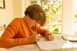 © Marc Romanelli - 12 year old boy doing homework at kitchen table at sunset