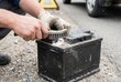 © Stitch - Mechanic using a metal wire brush to clean corrosion off the terminals of a black car battery