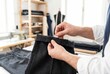 © Stitch - Tailor hands pinning the hem of dark grey trousers in a clothing workshop