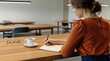 © Evarelle - Woman student writing in notebook at table with coffee cup. Girl education and learning concept. Desk setup in library or office workspace. Focused study, working and planning task.