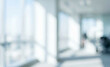 © birulaut - A soft-focus view of an office interior with bright sunlight streaming through large windows, creating a modern and airy atmosphere.