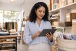 © Studio - Confident young professional woman using tablet in bright modern retail clothing store, focused on inventory management or digital catalog, casual business attire with light blue blouse and white