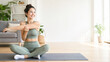 © Kowit - A woman in activewear smiles while stretching on a yoga mat in a bright, cozy living room.