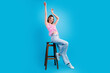 © deagreez - Happy young woman dancing on stool in pink top and jeans against bright blue studio background