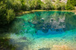 © Yuliko - Deep turquoise karst spring with crystal clear water reflecting green vegetation and rocky cliffs
