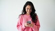 © miss irine - Young woman in pink sweater smiles looking at her phone. She is holding a mobile device and texting or browsing. This represents digital connection and happiness.