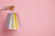 © Ольга Клецкова - Female hand holding colorful shopping bags on pink background retail sale and gift concept