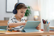 © New Africa - Little boy with headphones using modern tablet at wooden table indoors