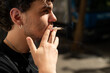 © dsbedarieva - Close up profile of a young man with curly hair and an earring smoking a cigarette outdoors in Paris.