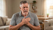 © vefimov - An older man sitting on a couch holding his chest with pain.