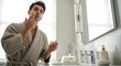 © SashaMagic - Young man applying face cream in a modern bathroom during his morning skincare routine, focusing on self-care and healthy skin.