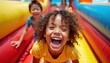 © Viktor - Joyful children laugh while sliding down a colorful inflatable attraction. Kids have fun with active play and exciting games on a summer day. Pure happiness and energetic childhood moments captured.