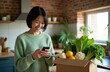 © Maryna - Asian woman smiles uses smartphone near box of fresh groceries. She unpacks vegetables and fruits in kitchen. Online food order delivery concept. Easy meal prep.