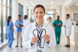 © Meow Creations - Smiling female doctor holding a black stethoscope formed into a heart shape in a hospital corridor