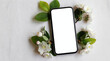 © Raisa - Clean smartphone rests on white fabric with delicate white blossoms and green leaves. Blank screen perfect for graphic design, app promotion or spring sale ads.