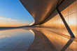 © jianhua - This minimalist curved architectural terrace captures warm golden hour sunset light, with reflective tiled floors and metal facade panels mirroring the warm sky tones.