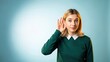 © MT - Young woman listening intently with hand to ear on blue background