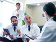 © .shock - Middle Eastern doctors consulting in hospital clinic meeting reviewing patient records with tablets and notes