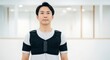© QuiinL - A man wearing a black posture-correcting vest stands in a brightly lit room, looking directly at the camera.