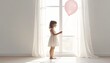 © hyena - Young Child Holding Pastel Balloon Beside Bright Sunlit Window Indoors