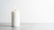 © EsterDyah - A burning pillar candle stands isolated on a plain white background surface.