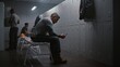 © Framestock - Tattooed Male Worker Sits on Grey Bench in Modern Industrial Locker Room, Using Smartphone to Make Call While Coworkers Undress After Factory Shift. Concept of Connecting With Home During Break.