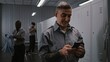 © Framestock - Muscular Male Security Officer With Tattoos at Locker Hangs Up ID, and Uses Smartphone to View Notifications and Social Media After Long Airport Security Shift. Workplace Communication Concept.