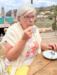 © luciano - Elderly Woman Enjoying Coffee At Outdoor Beachside Cafe Wearing Light Sweater And Glasses