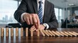 © Myimages - Businessman hand stopping falling domino blocks, preventing chain reaction, symbolizing risk management, crisis control, and leadership strategy