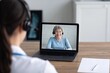 © oksa_studio - Doctor wearing headset, interacting with an older woman on laptop, providing remote healthcare consultation and online support