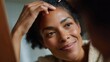 © GATE 22 - Close-up portrait of a young african-american woman with short curly hair. she is looking at her reflection in the mirror with a smile on her face.