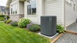 © DailyStock - Residential central air conditioning unit installed on a concrete pad next to a house with beige siding and stone accents in a garden setting