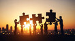 © zaaf - Silhouette of a team of people assembling jigsaw puzzle pieces together against a sunset cityscape backdrop, symbolizing teamwork and collaboration for achieving a common goal