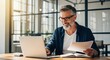© twilight mist - Mature man working on a laptop at an office desk while holding a document.