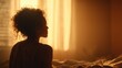 © Selvi - Silhouette of a woman sitting on bed in warmly lit bedroom with curtains
