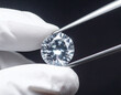 © Sultana khatun - A sparkling round cut diamond gemstone held by silver tweezers with white gloved hands against a dark background