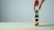 © DAS - A hand places a block with a smiley face on top of three blocks with icons on a wooden table against a plain background.