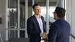 © fizkes - Two businessmen greeting each other with handshake standing in office hallway. Successful collaboration, agreement, client and manager relations, positive business communication and partnership sign