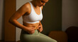 © HAKOBYAN ANAHIT - Woman in fitness wear pinching stomach fat while sitting. Female athlete checking her body composition and belly area. Body positivity and weight loss concept for health and nutrition marketing.
