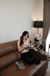 © Parichat - Young woman writing notes working on sofa