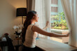 © Parichat - Woman opening curtains seeing new day rising with sunshine